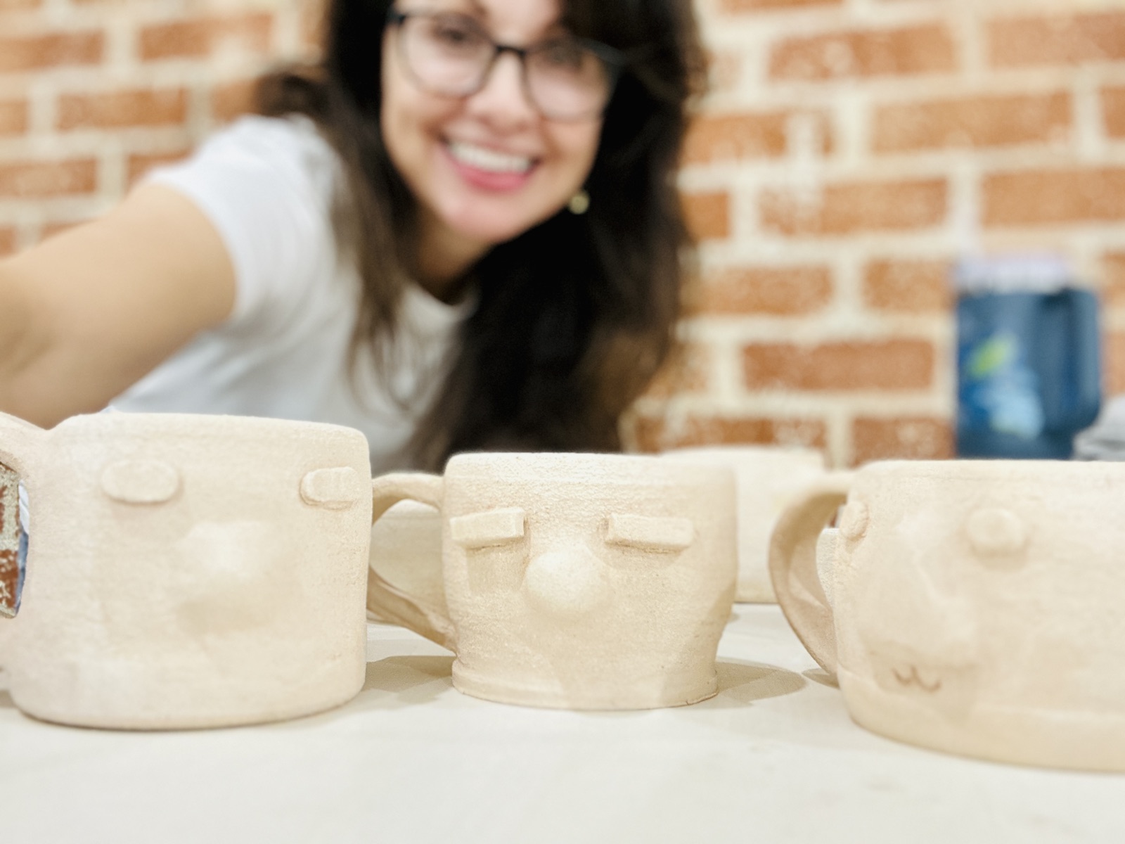 Three hand-built mugs with little faces, Suzanne smiling behind them